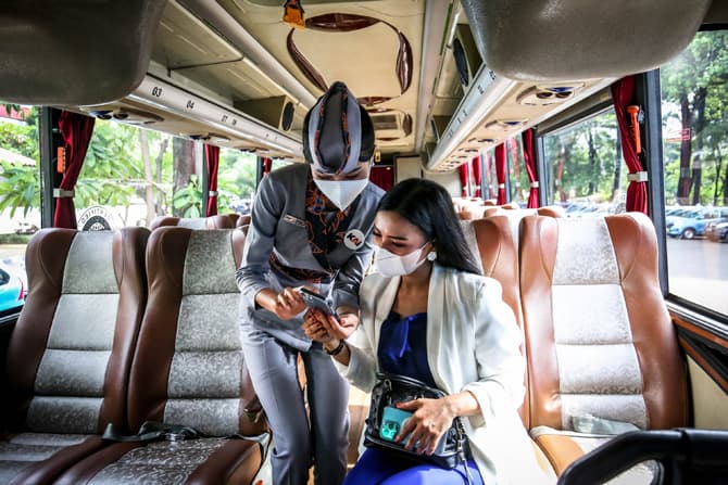Pramugari menjelaskan kepada calon penumpang tentang aplikasi layanan antarmoda Kereta Api Jarak Jauh dengan Bus DAMRI di Stasiun Gambir, Jakarta, Rabu(2/1/2022).PT Kereta Api Indonesia (Persero) bekerja sama dengan Perum DAMRI untuk menghadirkan layanan - Image
