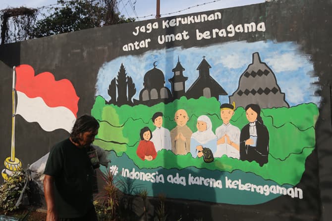 Warga melintas di depan mural kerukunan umat beragama di kawasan Beji, Depok, Jawa Barat, Senin (4/7/2022). Mural tersebut sebagai media edukasi kepada masyarakat agar selalu menjaga toleransi dan persatuan bangsa meskipun berbeda suku dan agama untuk me - Image
